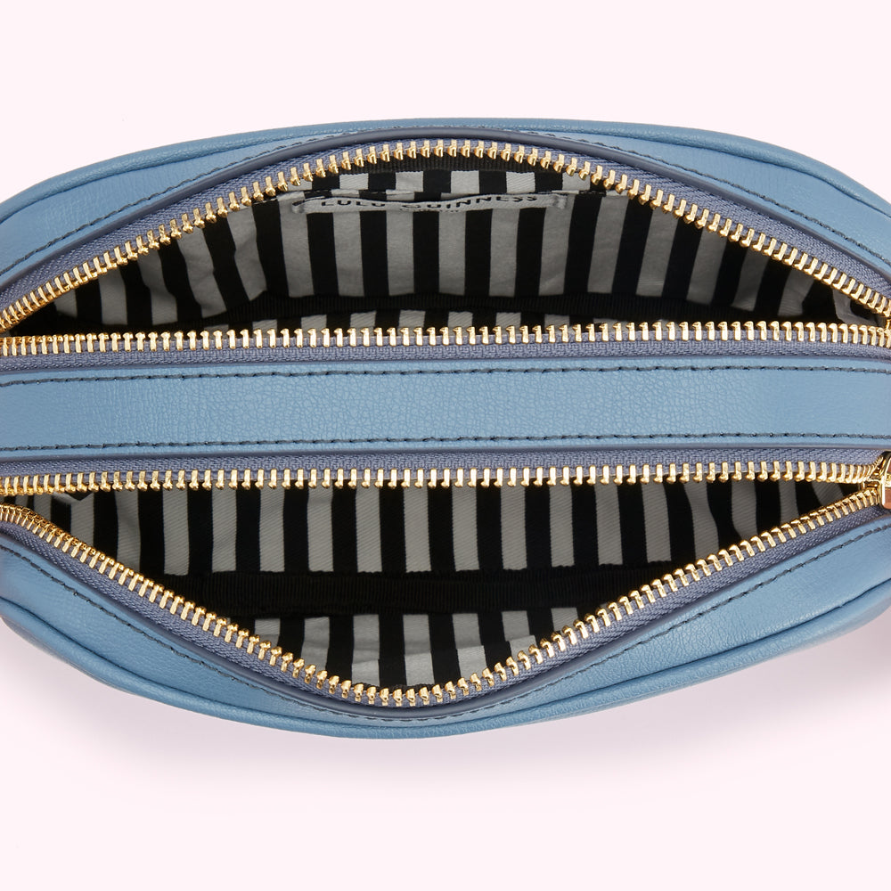 Inside of a light blue, oval-shaped crossbody bag with gold zippers and a black and white striped interior.
