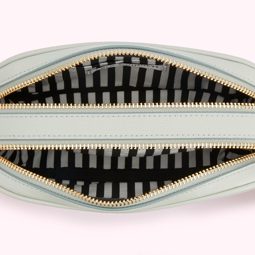 Interior of a light blue crossbody bag with gold zippers and a black and white striped lining.
