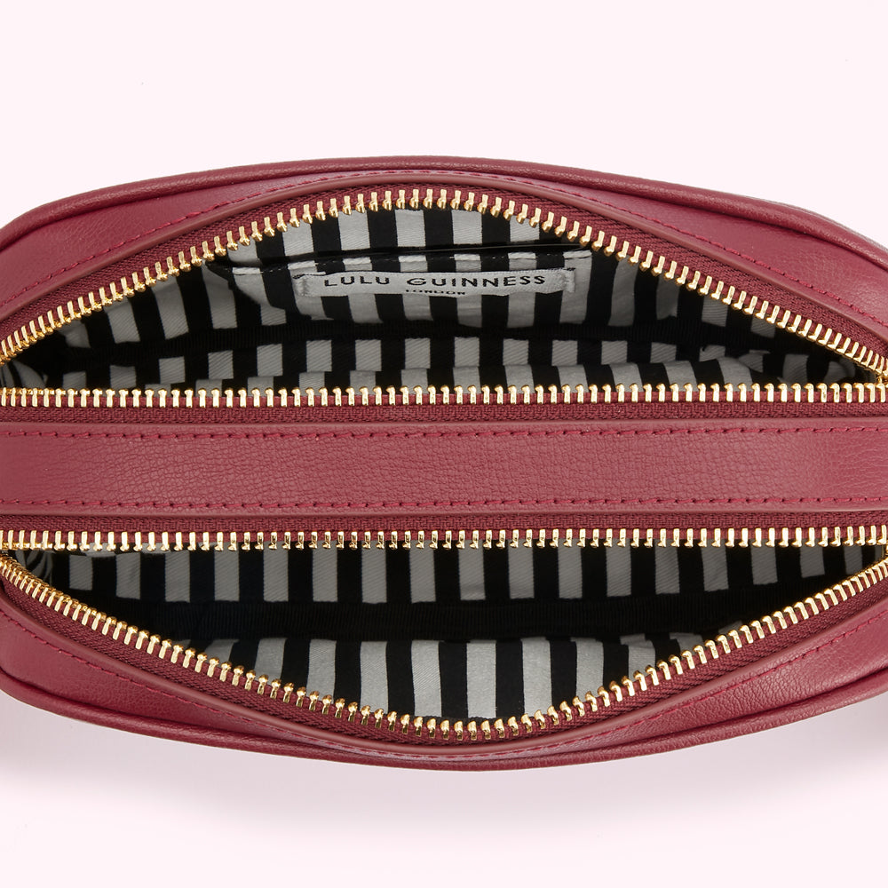 Inside of a Lulu Guinness burgundy leather crossbody bag with gold zippers and a black and white striped lining.
