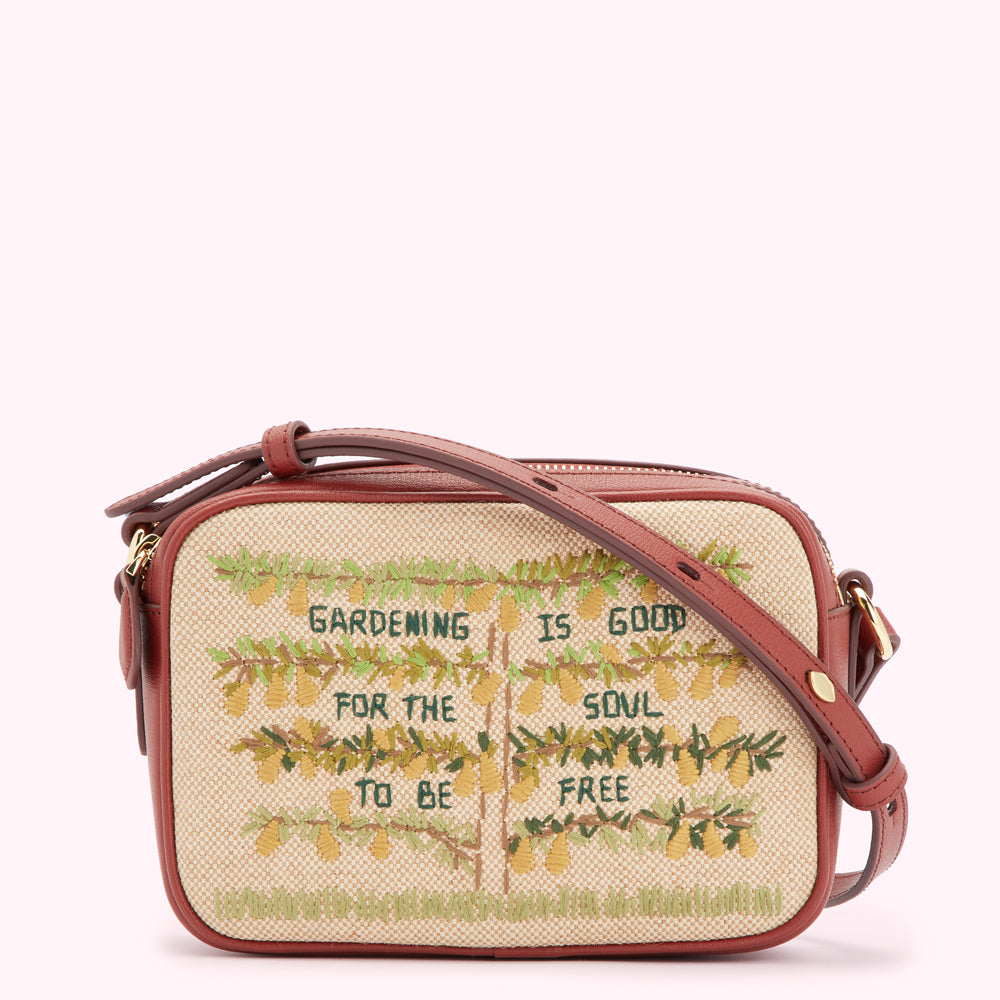 Beige crossbody bag with brown leather strap, embroidered with trees and the text "Gardening is good for the soul to be free".
