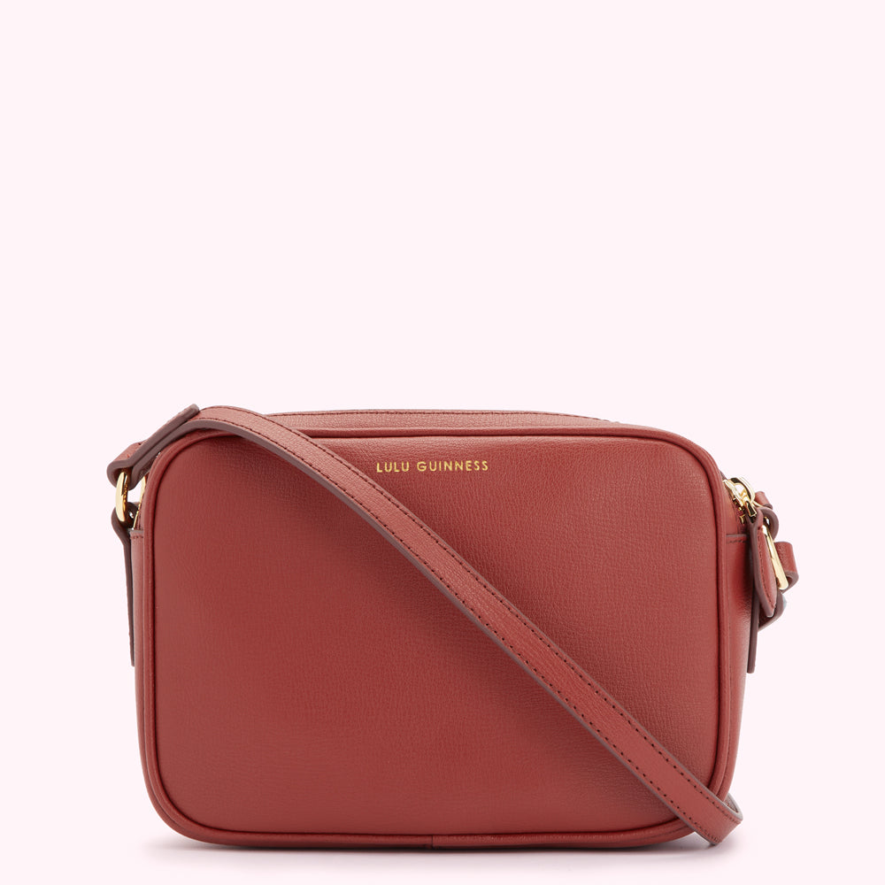 A burnt orange Lulu Guinness crossbody bag with a long strap.

