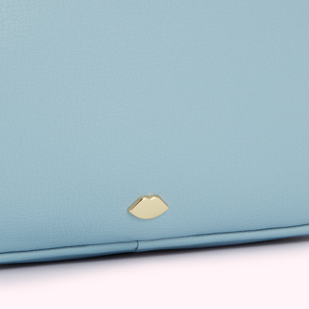 Close-up of a light blue leather purse with a gold lip-shaped emblem.
