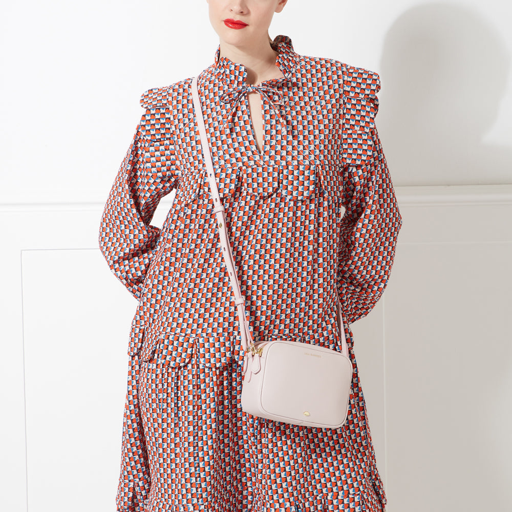 A woman in a geometric print dress carries a pale pink crossbody bag.
