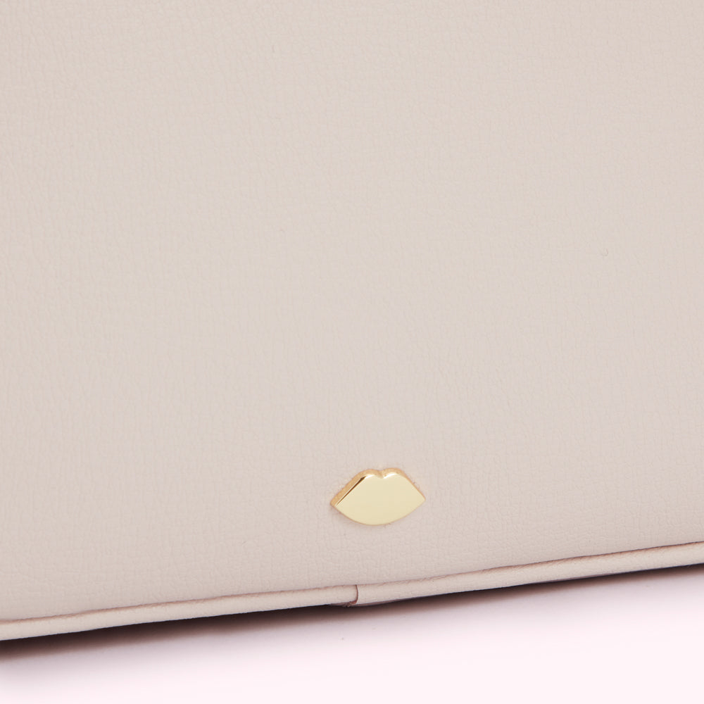 Close-up of a pale beige leather bag with a small gold lip-shaped emblem.

