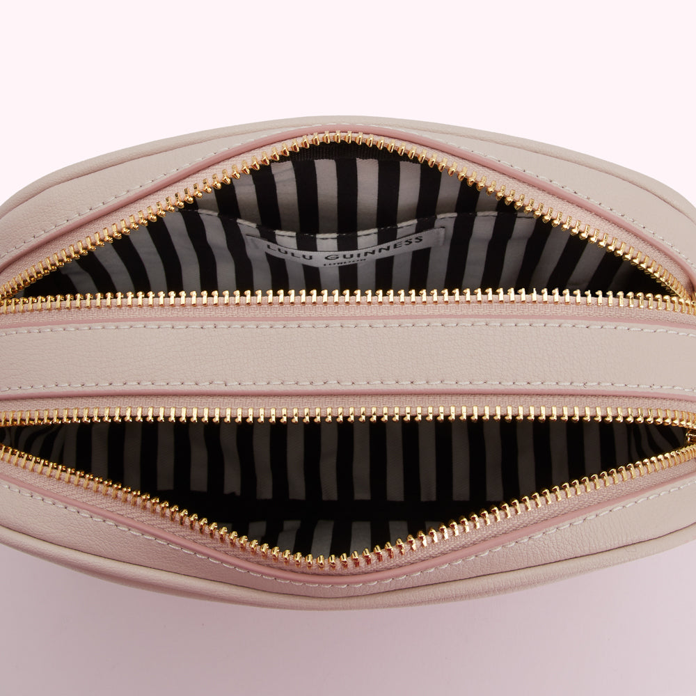 Interior of a pale pink Lulu Guinness crossbody bag with a black and white striped lining and gold zippers.
