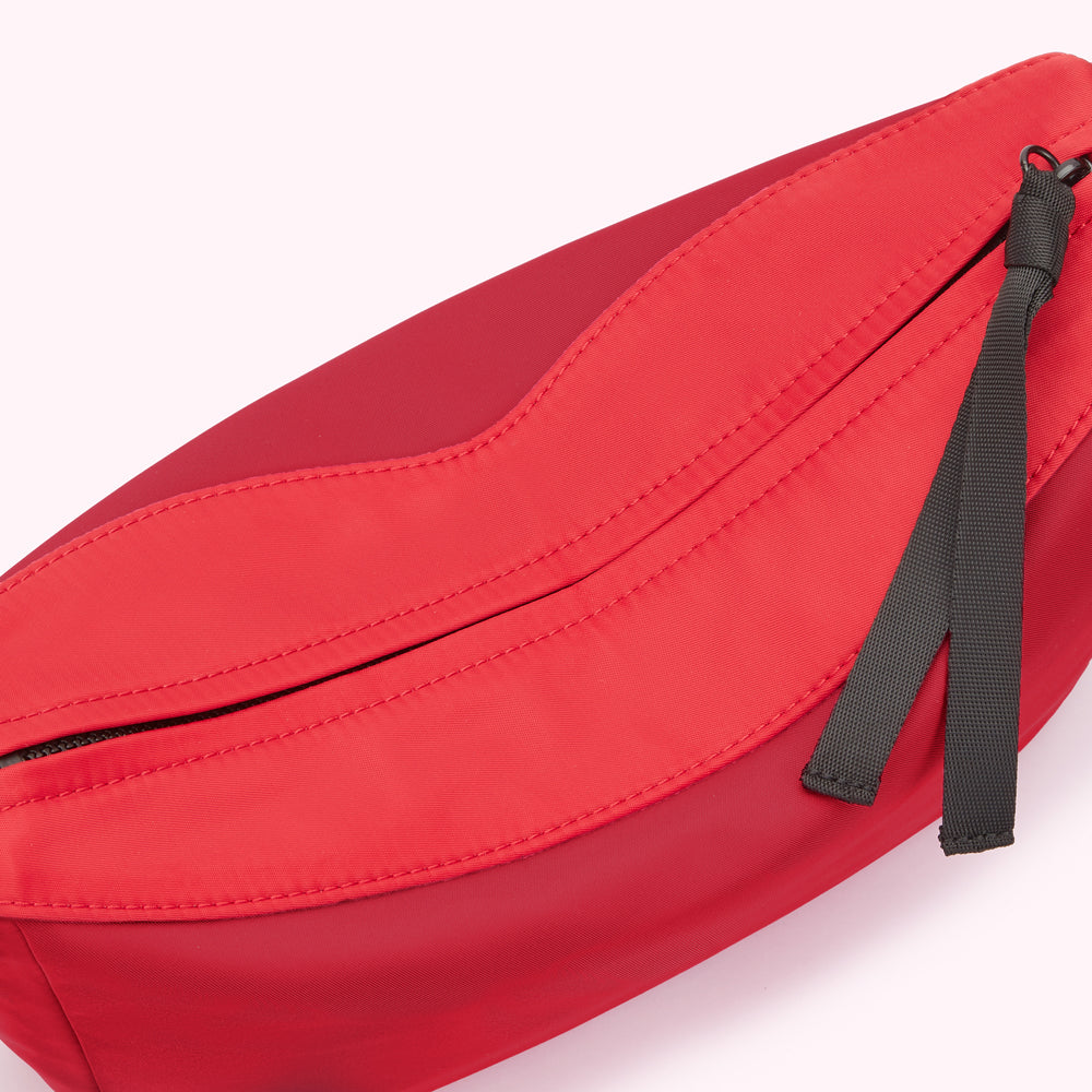 Close-up of a red nylon crossbody bag zip with black ribbon zip pull.