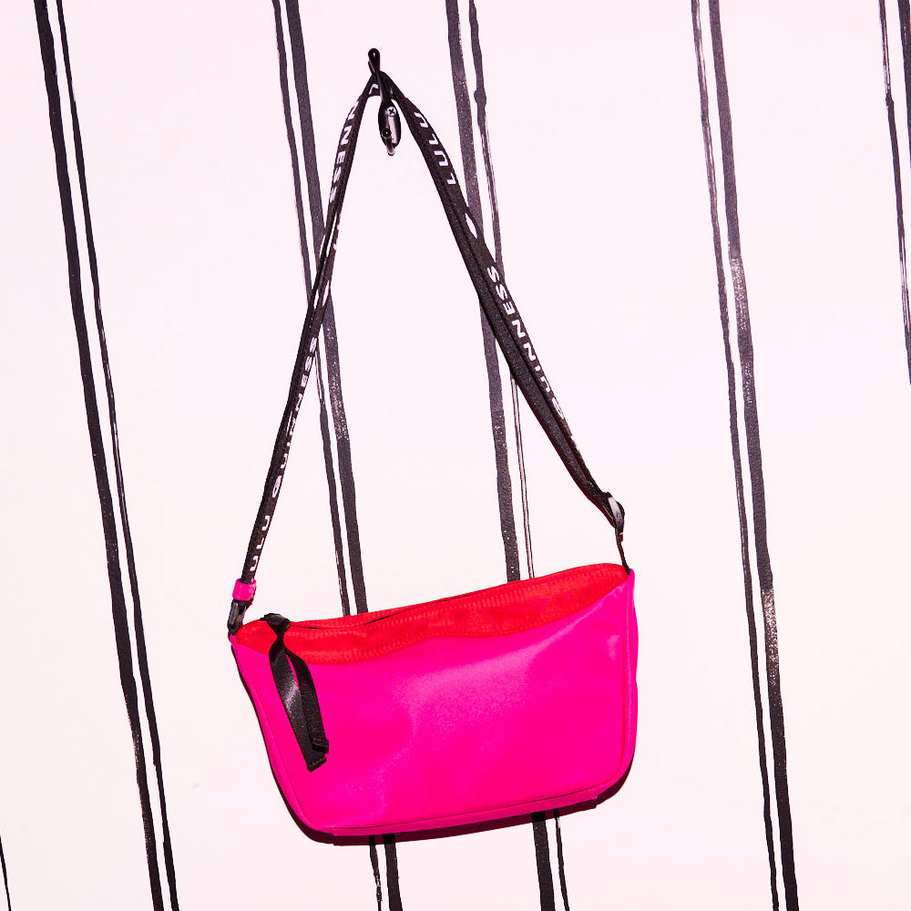 Hot pink nylon shoulder bag with a branded 'Lulu Guinness' strap handing on a hook.