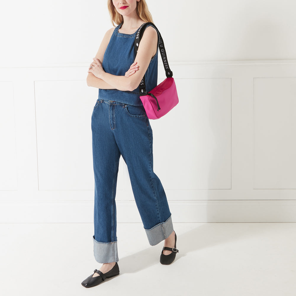 Model in a denim outfit and red lipstick wearing a bright pink and red nylon shoulder bag with branded 'Lulu Guinness' shoulder strap.