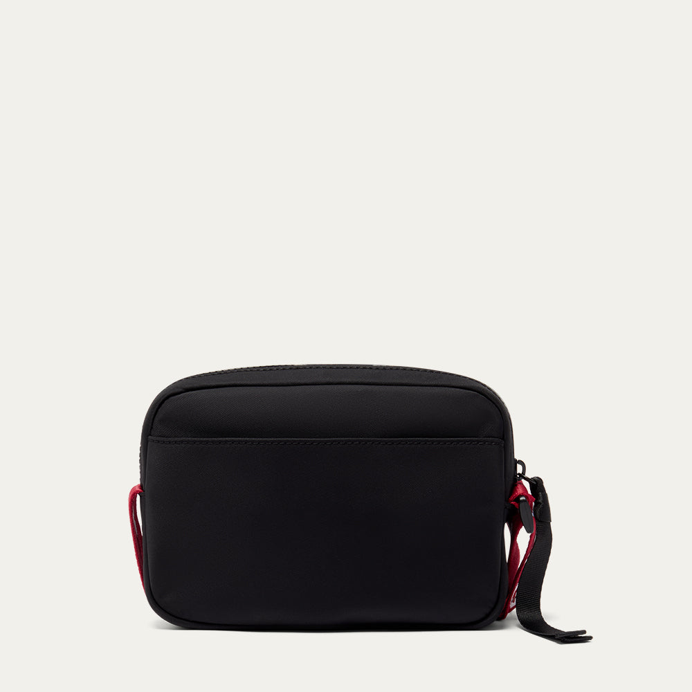 Black crossbody bag with red accents on a light grey background