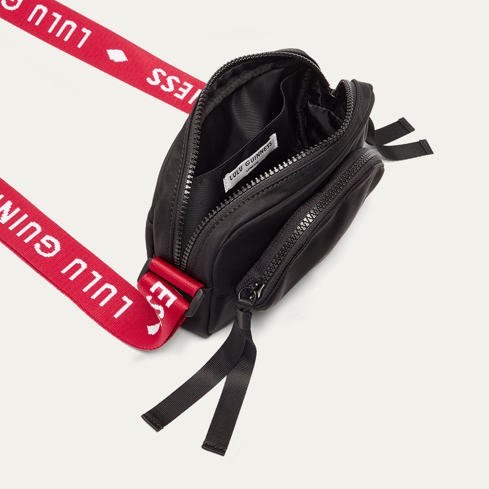 Black crossbody bag with a red branded 'Lulu Guinness' strap open on a white background