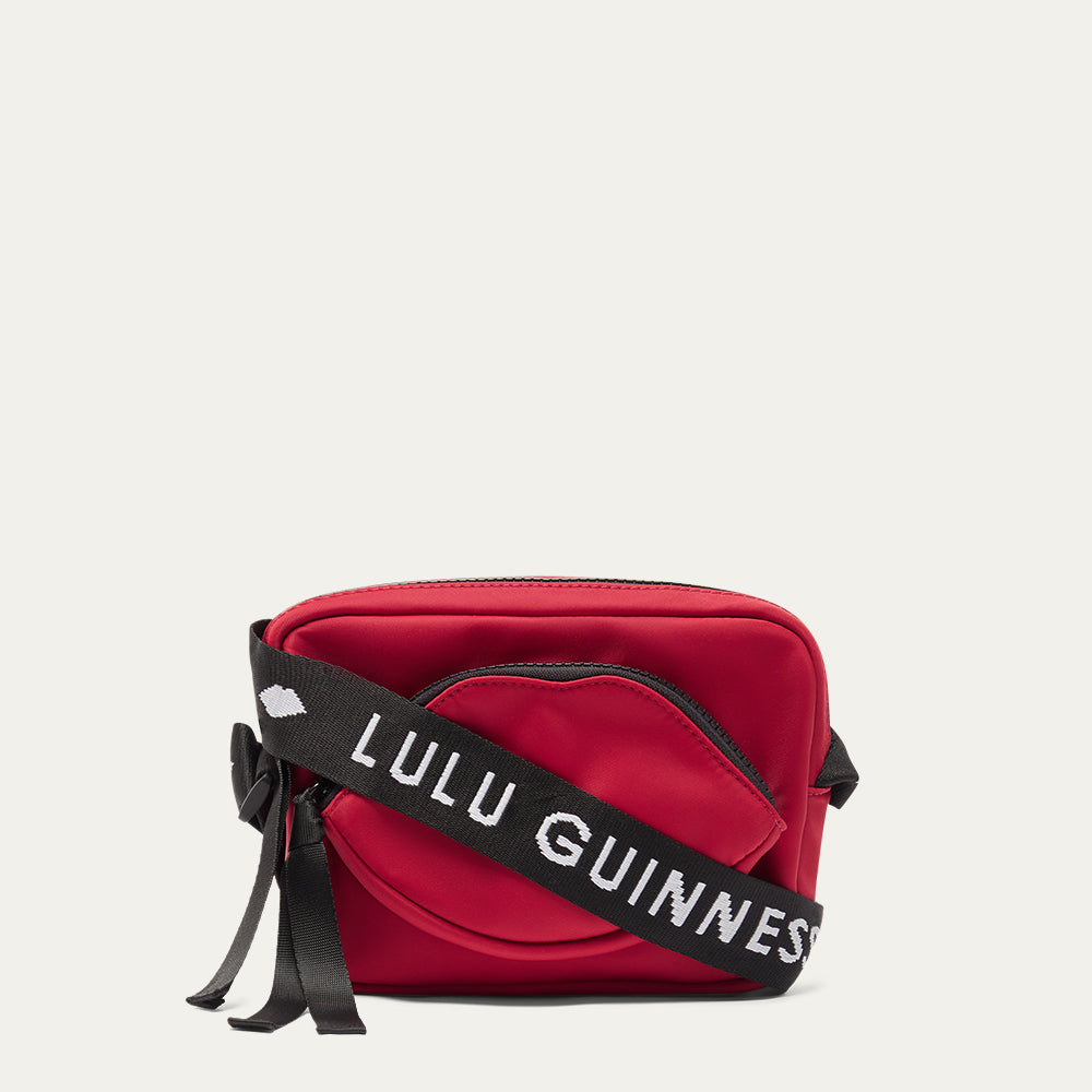 Red crossbody bag with a black strap featuring 'Lulu Guinness' on a light grey background