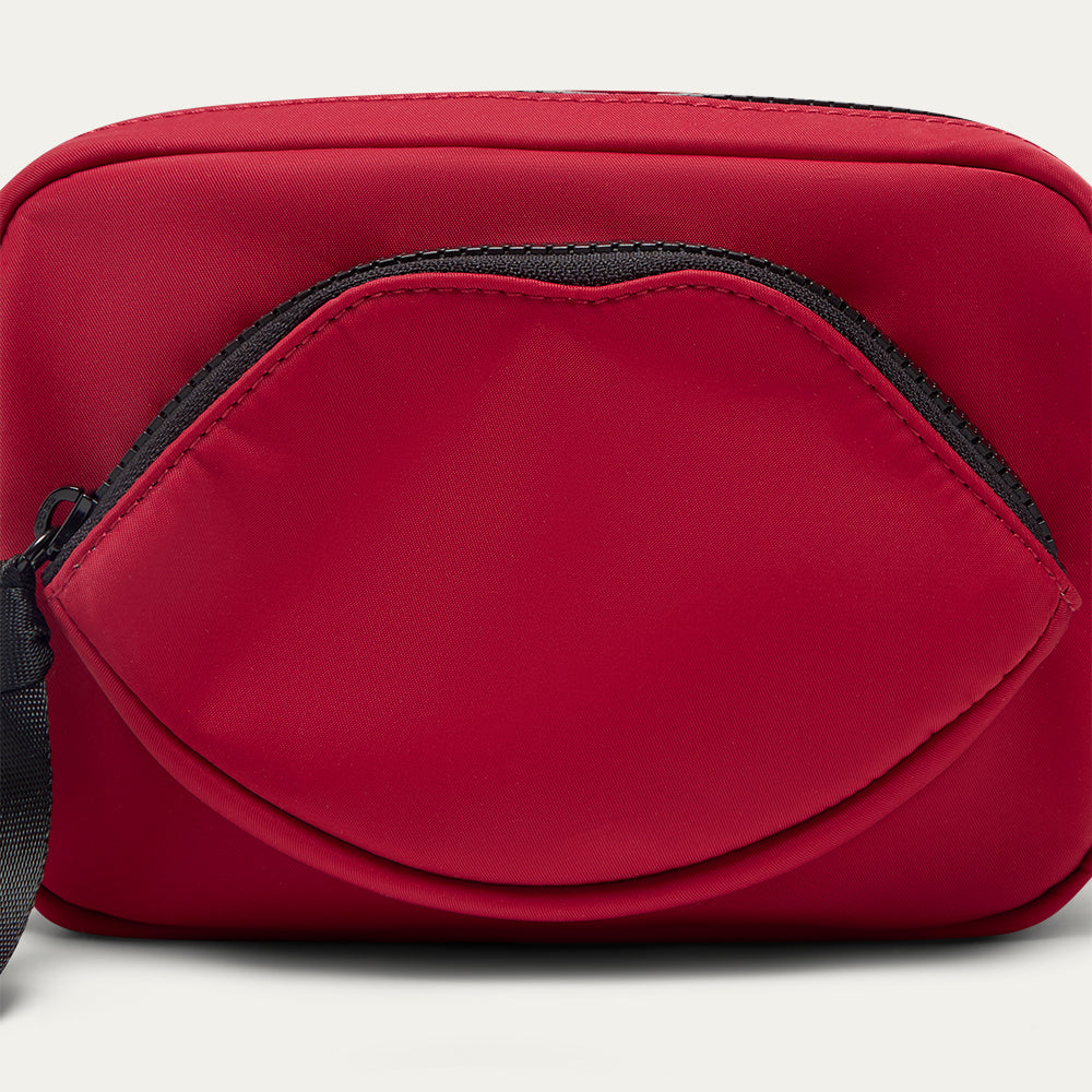 Close up image of a red crossbody bag with a lip-shaped pocket on a light grey background