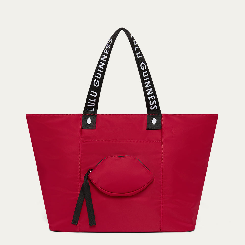 Red tote bag with black handles featuring 'Lulu Guinness' and a lip-shaped pocket on a light grey background