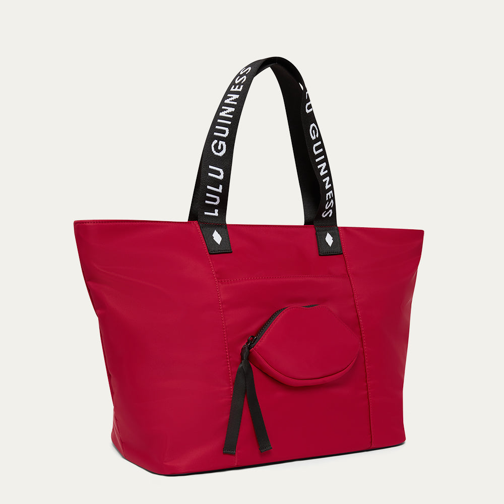 Red tote bag with black handles featuring 'Lulu Guinness' and a lip-shaped pocket on a light grey background