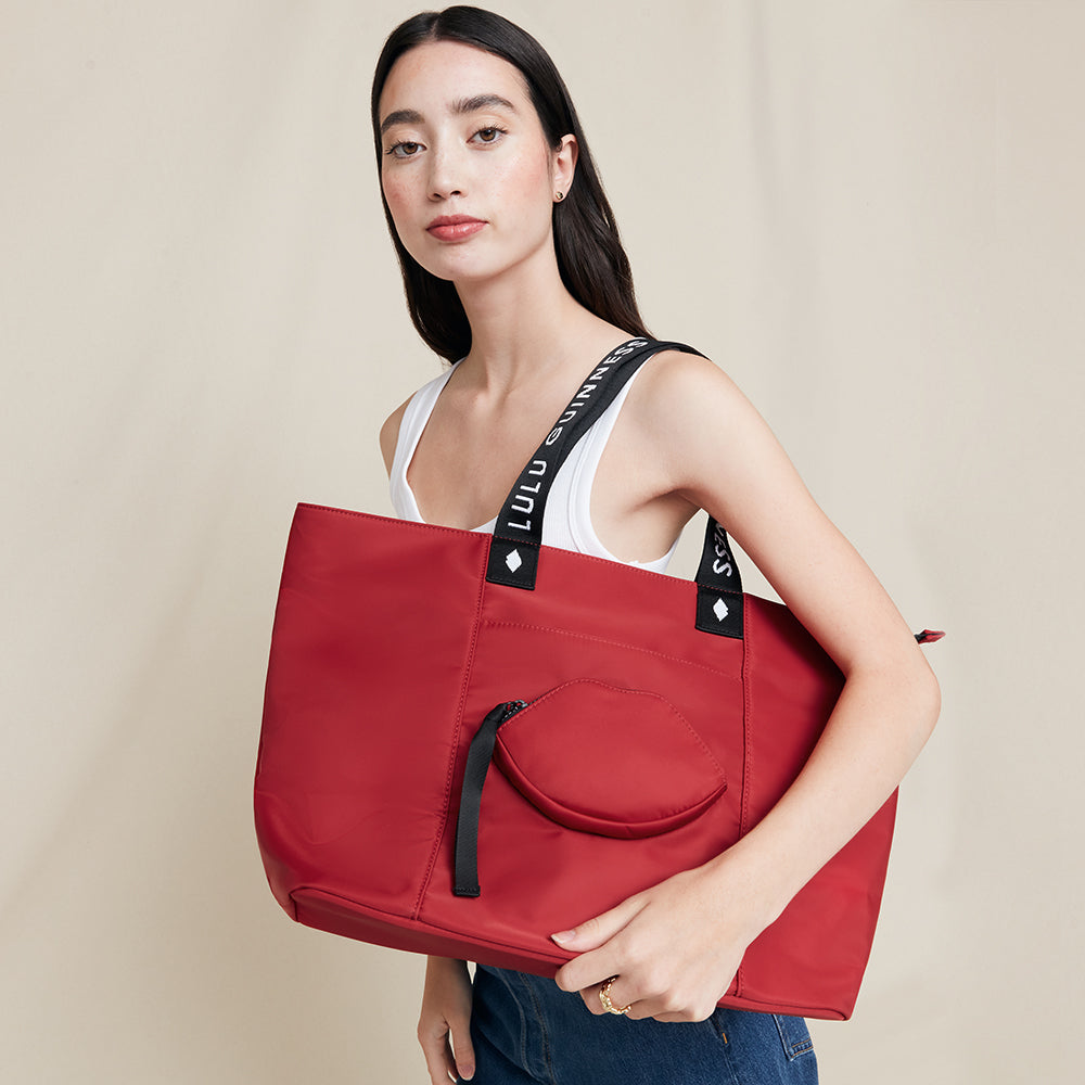 Woman holding a red tote bag with 'Lulu Guinness' branding on a beige background