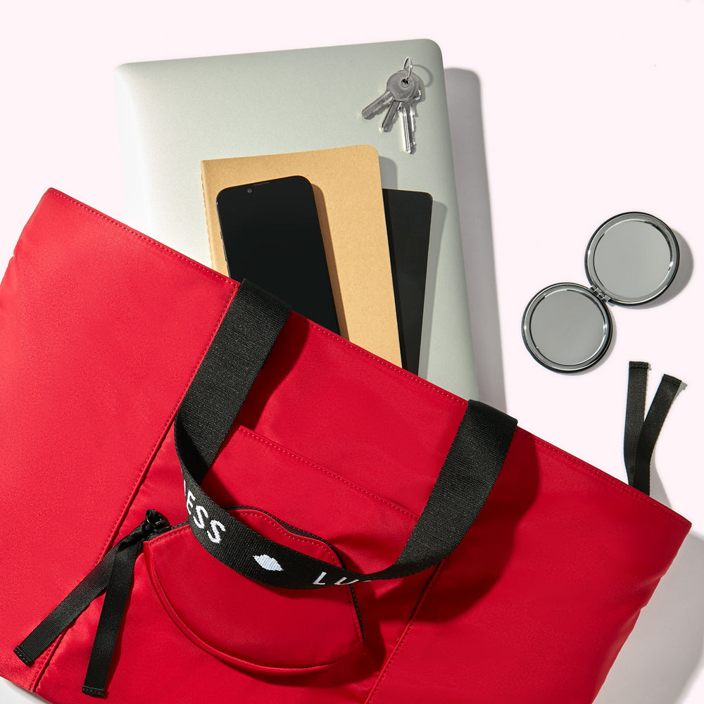 A red nylon tote bag handbag with a laptop, notebooks, smartphone, keys and compact mirror spilling out