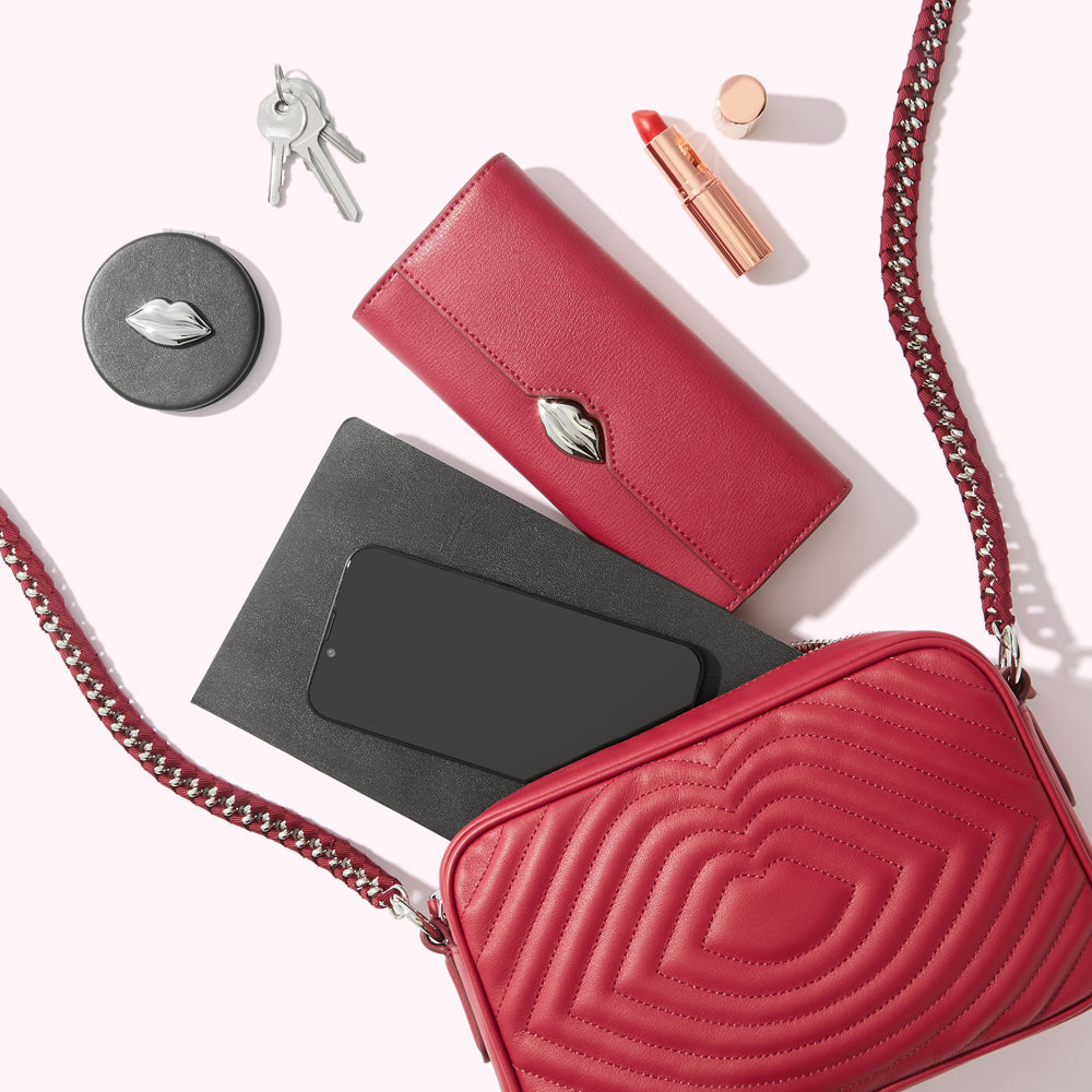 Red quilted crossbody bag with a red leather wallet, a smartphone, a compact mirror, lipstick, and keys inside.
