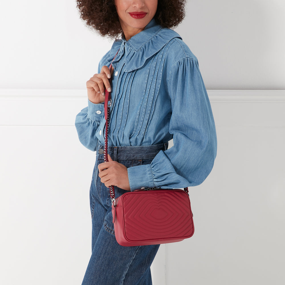 Woman in denim shirt holding a red quilted crossbody bag with a silver chain strap.
