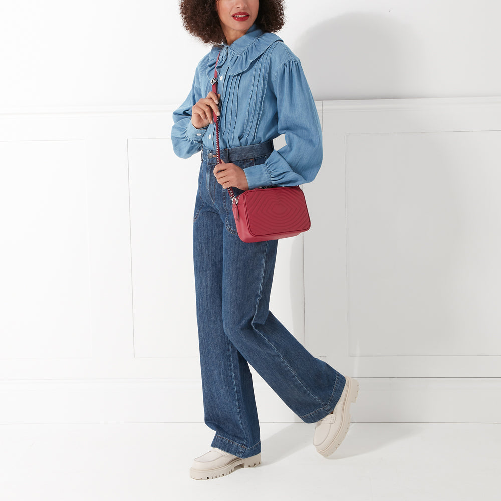 A woman in denim jeans and a light blue shirt carries a red quilted crossbody bag.