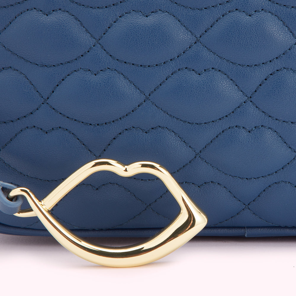 Close-up of a dark blue quilted handbag with a gold lip-shaped detail.
