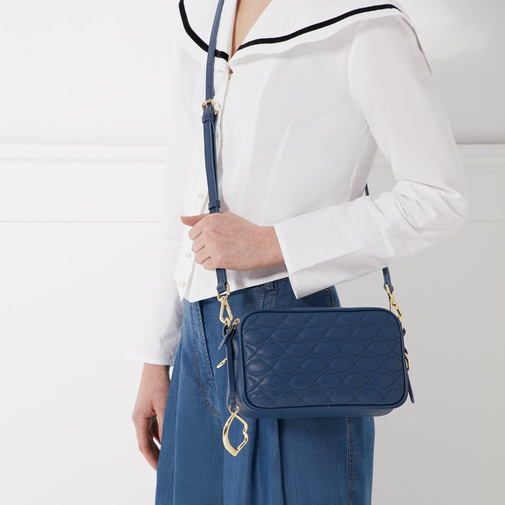 Woman wearing a white shirt and blue denim skirt carrying a quilted navy blue crossbody bag with gold accents.
