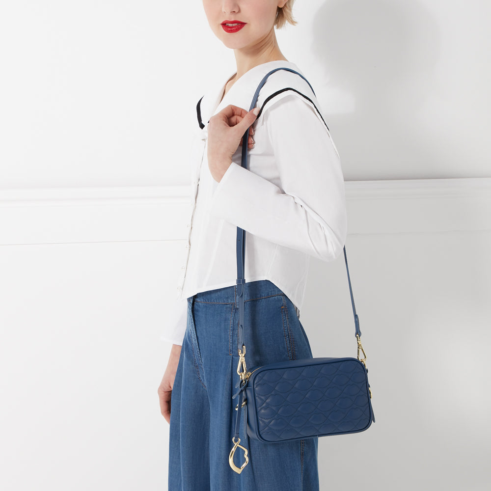 A woman in a white shirt and blue jeans holds a dark blue quilted crossbody bag.
