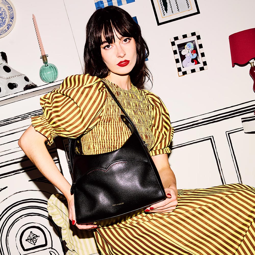 Model with dark hair wearing a yellow striped dress and holding a black leather shoulder bag.