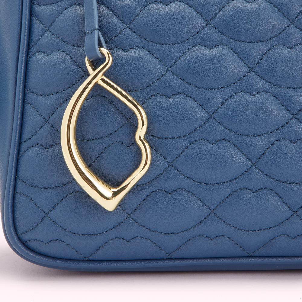 Close-up of a blue quilted handbag with a gold charm.
