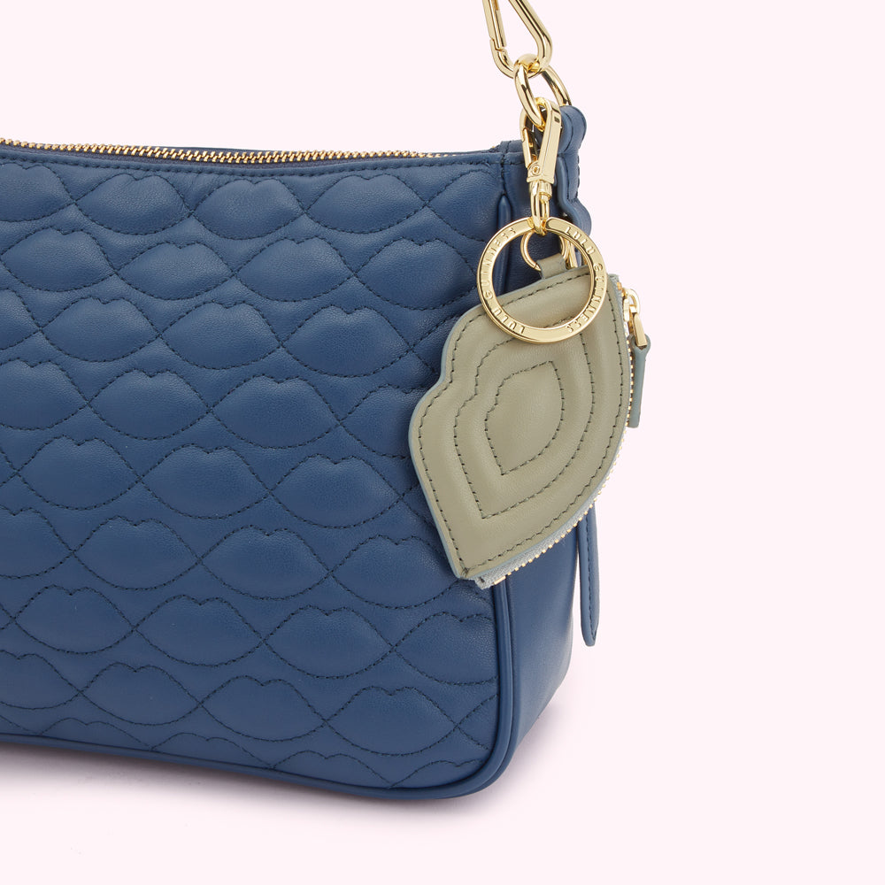 Close-up of a dark blue quilted crossbody bag with a lip-shaped charm attached.