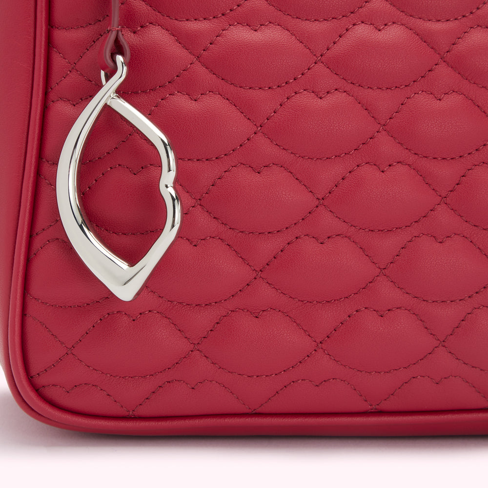 Close-up of a red quilted leather handbag with a silver lip-shaped charm.
