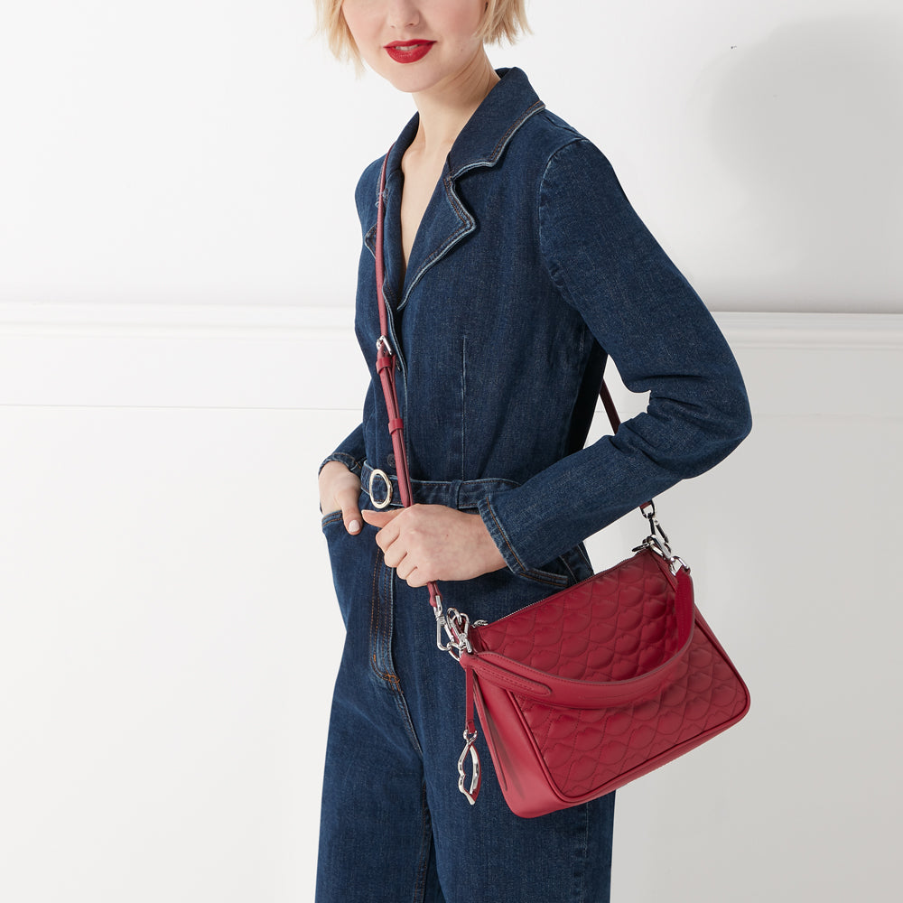 Woman in denim overalls holding a red quilted crossbody bag.
