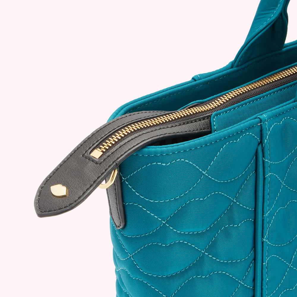 Close-up of a teal quilted handbag's zipper and top handle.
