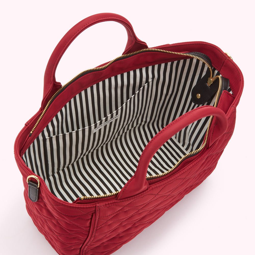 Open red quilted designer tote bag with dual handles, gold-tone zipper, and an interior lined with black and white striped fabric, displayed against a light pink background.