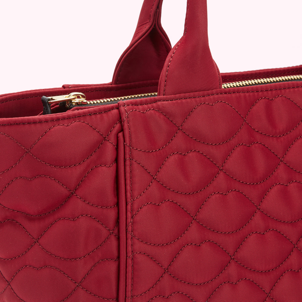 Close-up of a dark red quilted handbag with gold zipper and black handles.