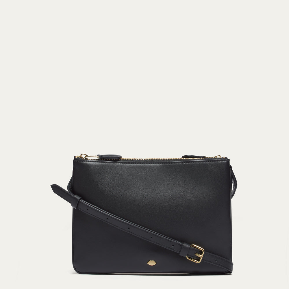 Black leather crossbody bag with gold lip pin on a light gray background