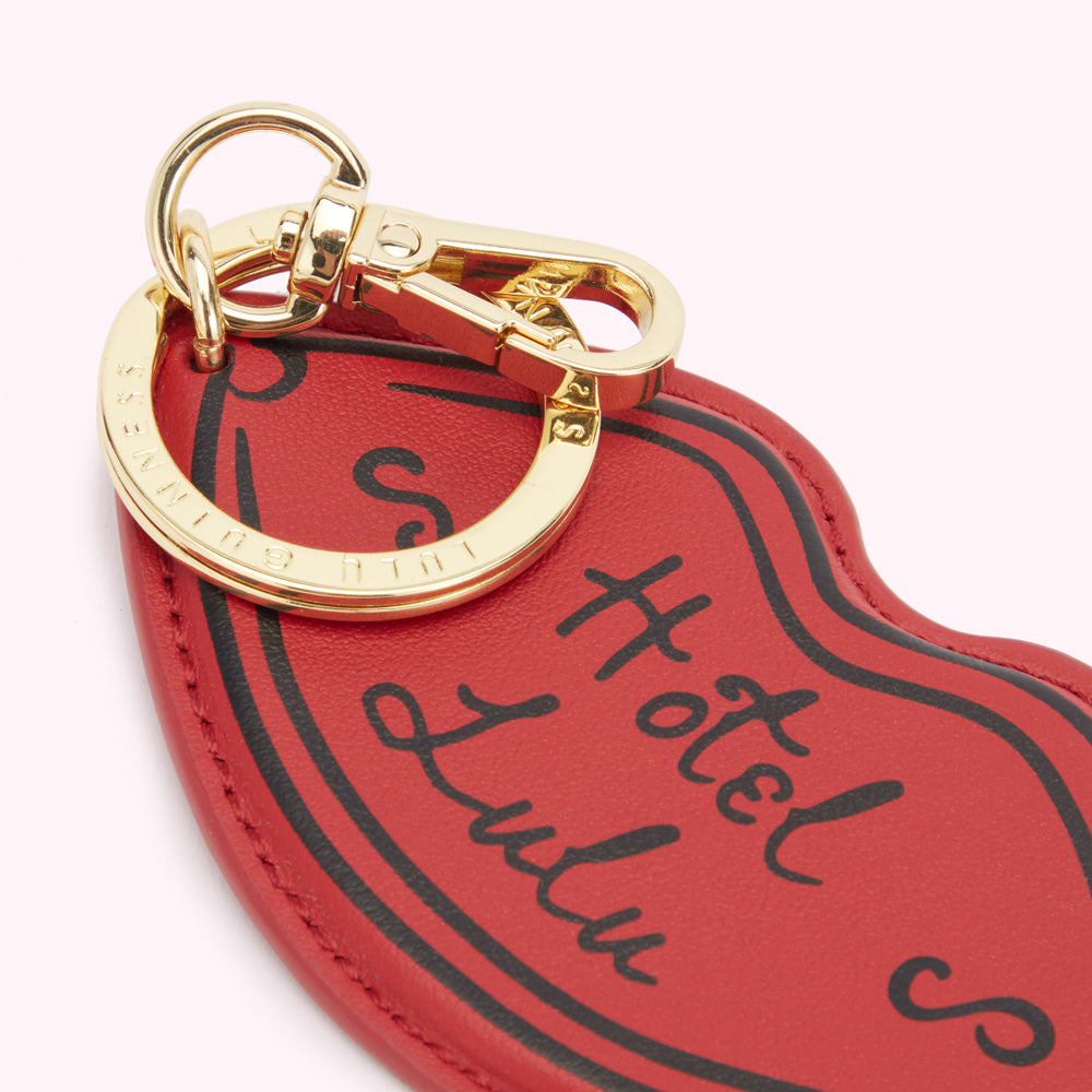 Detail image of a red leather lip shaped keyring showing the 'Hotel Lulu' print on the front and branded clip and ring fastening.