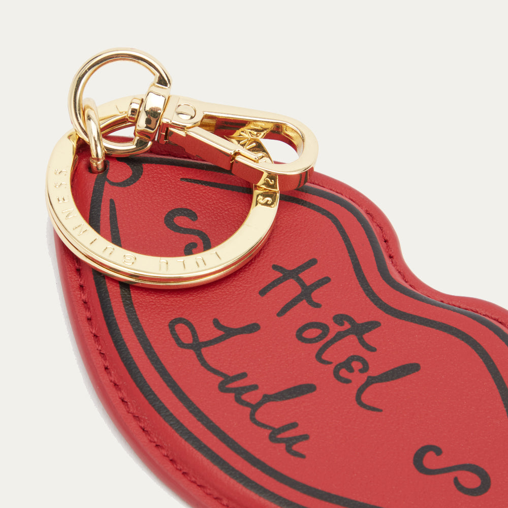 Detail image of a red leather lip shaped keyring showing the 'Hotel Lulu' print on the front and branded clip and ring fastening.
