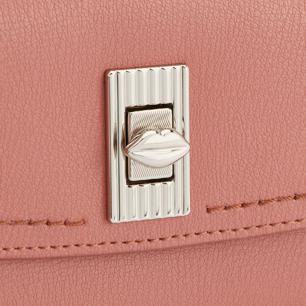 Close-up of a dusty rose handbag's clasp, featuring a lip-shaped detail.

