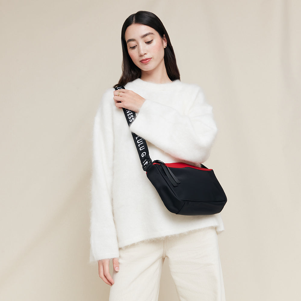 Woman wearing a black crossbody bag with red panel on a beige background