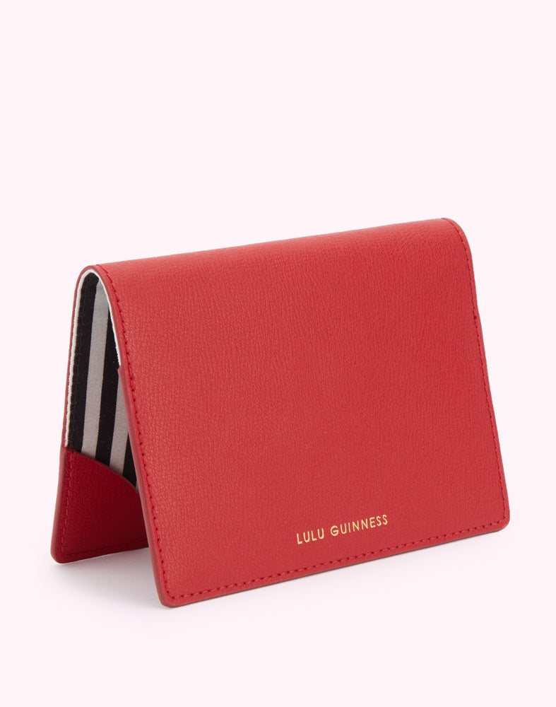 A back image of a red leather passport cover with a gold foil 'Lulu Guinness' logo.
