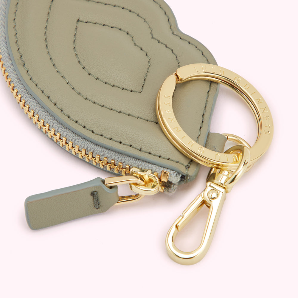 Close-up of a sage green Lulu Guinness coin purse with gold zipper and keyring.