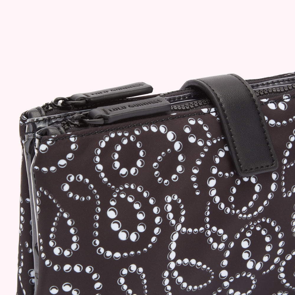 Close-up of a black Lulu Guinness zip-top pouch with a white pearl pattern and black leather strap.
