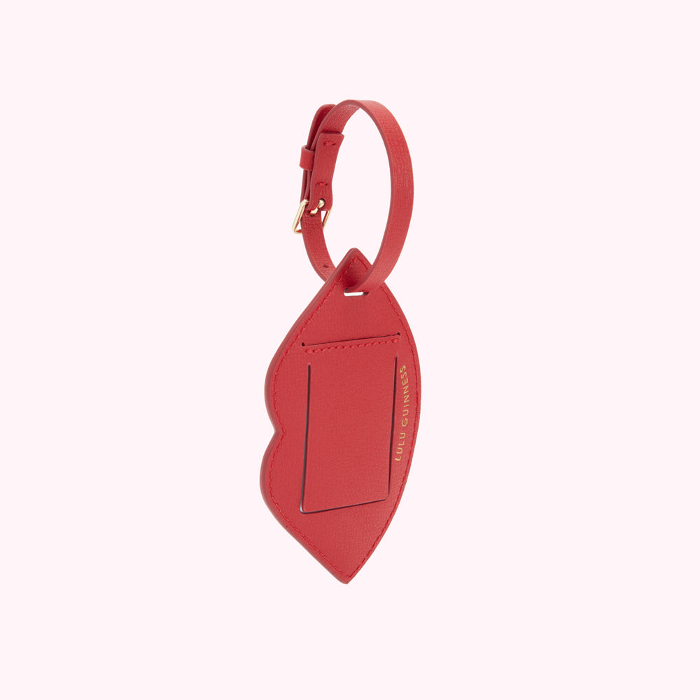 A back image of a red leather luggage tag with buckle fastening and a foil print 'Lulu Guinness' logo.