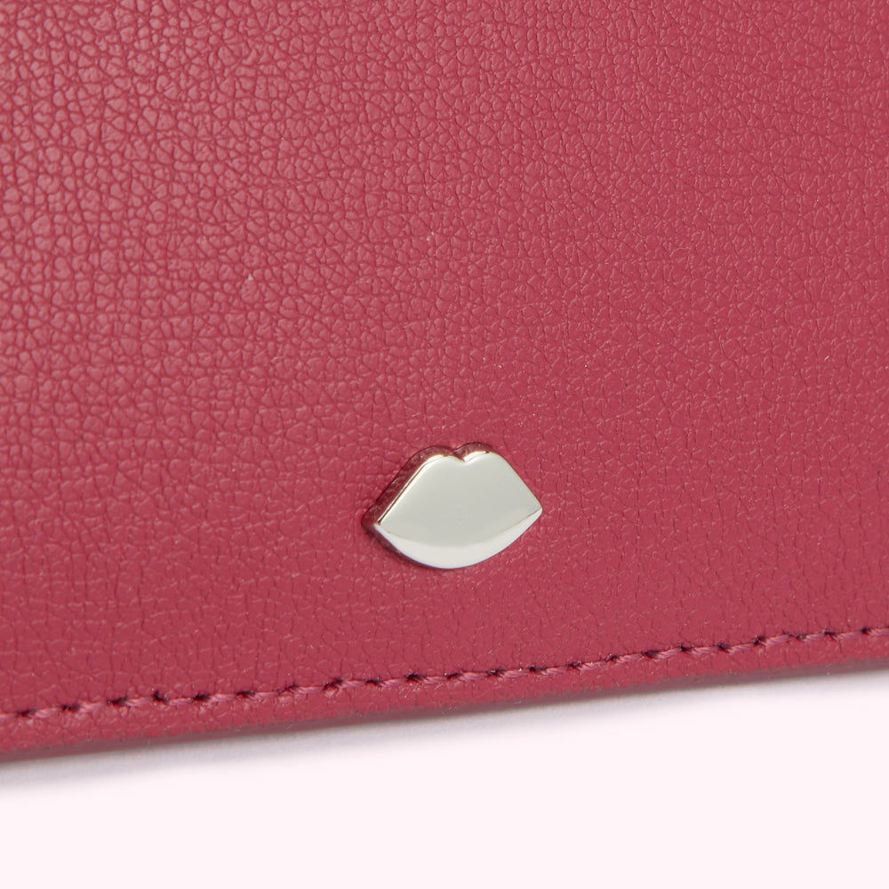 Close-up of a dark pink leather wallet with a silver lip-shaped emblem.
