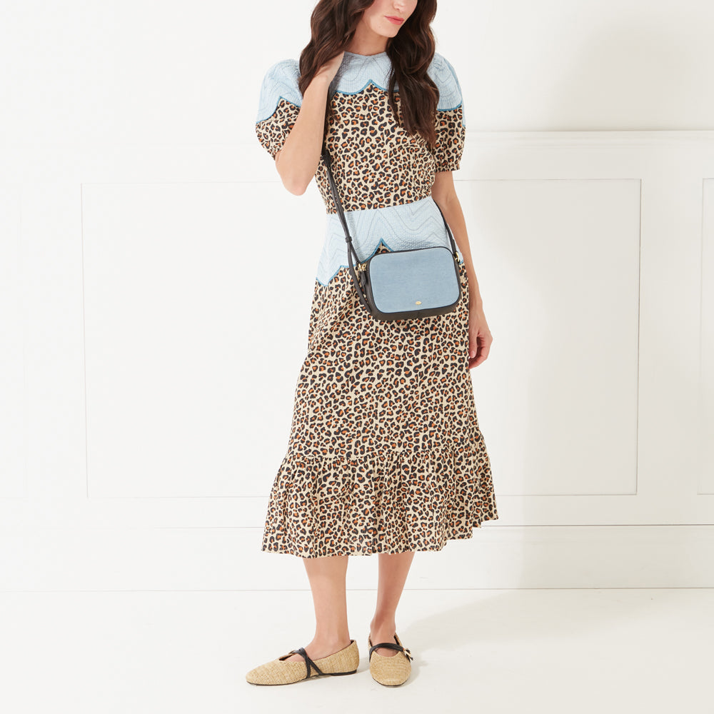 Model with dark hair and red lipstick wearing a leopard print dress and a denim crossbody bag.