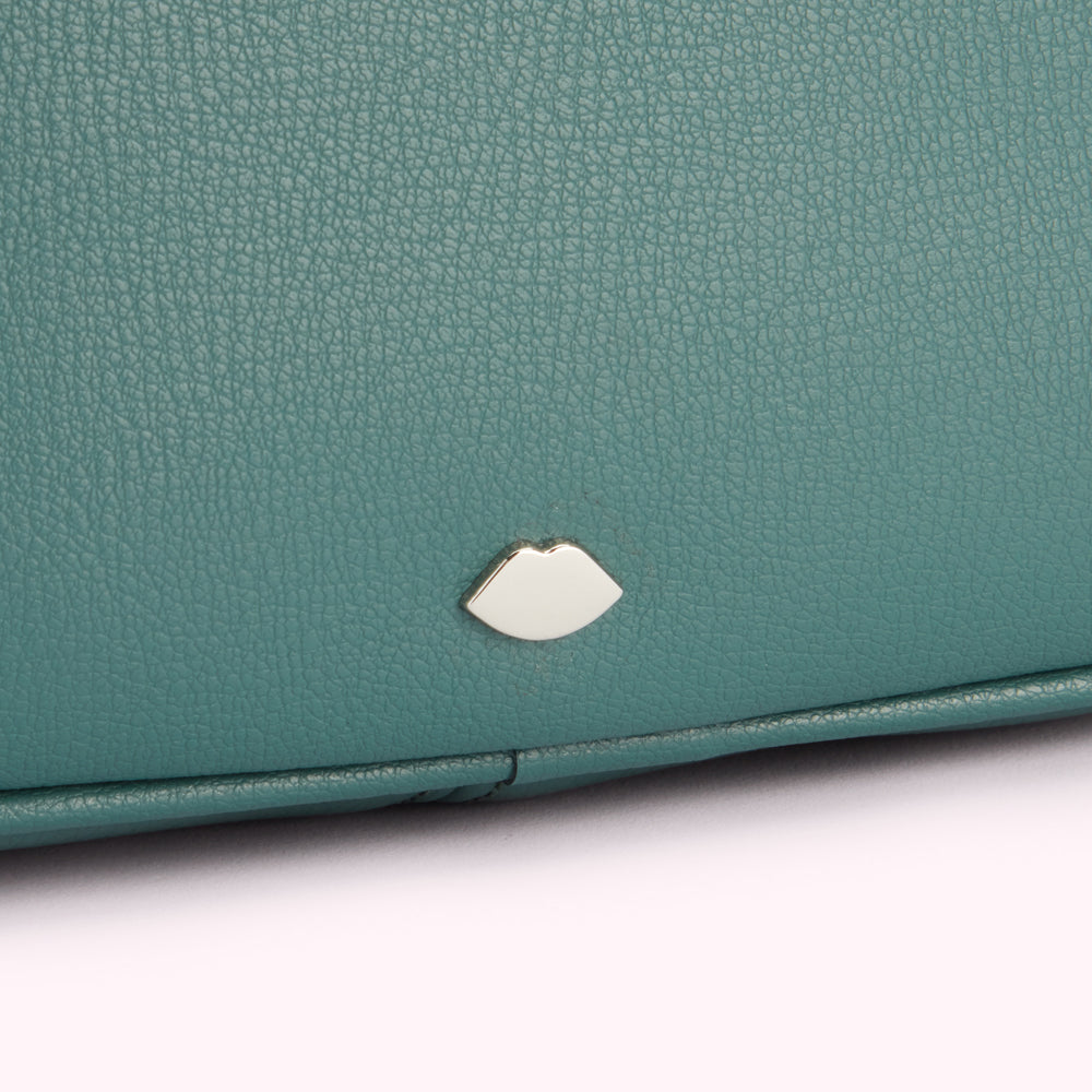 Close-up of teal textured leather with a silver lip-shaped emblem.
