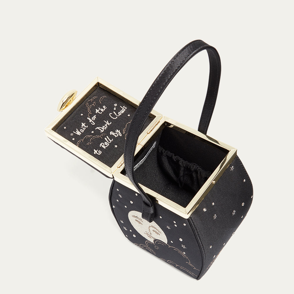 Black satin handbag with gold accents and decorative elements on a light gray background
