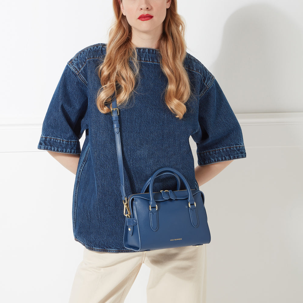 Woman in denim shirt holding a navy blue Lucy Guinness handbag.
