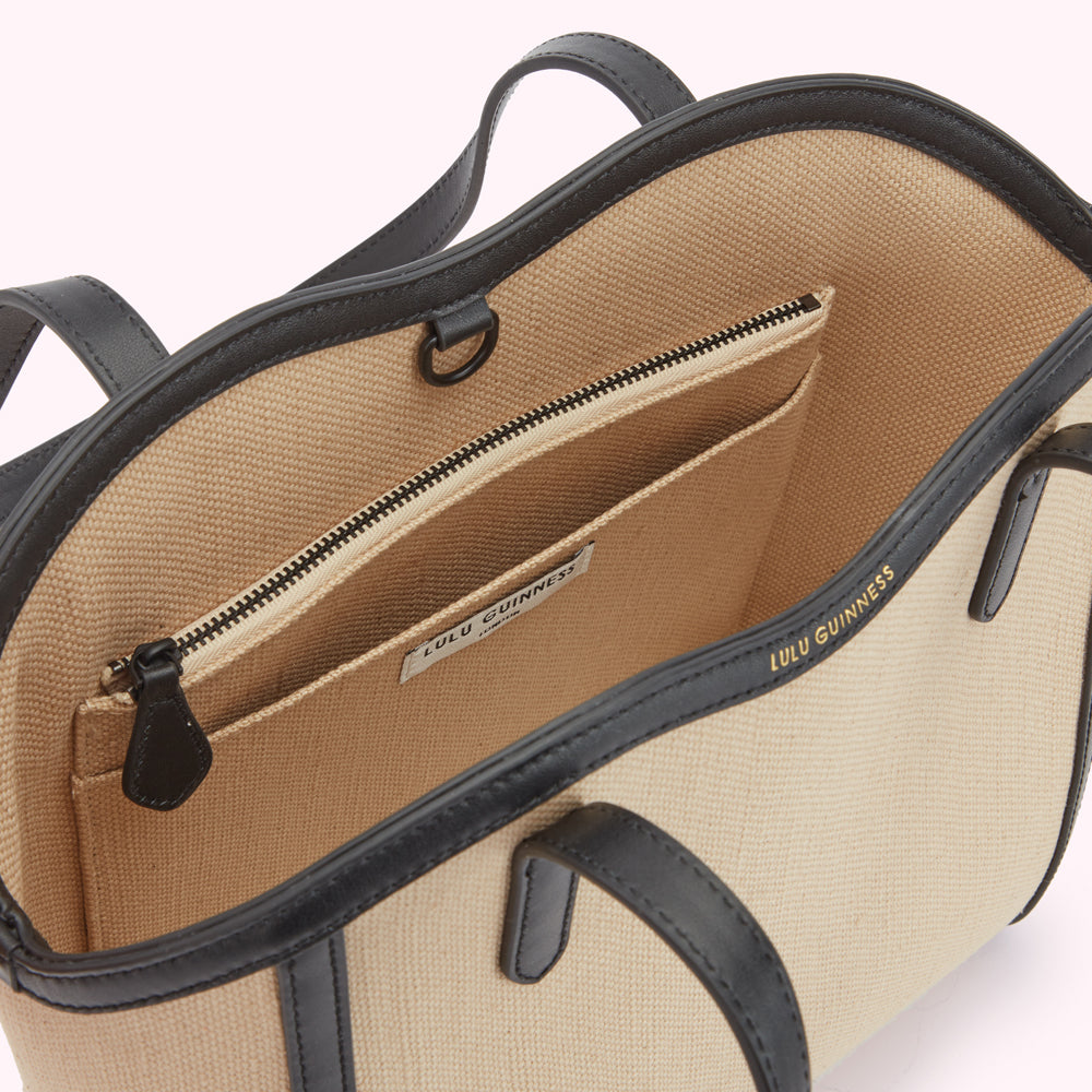 A inside image of a beige canvas and black leather tote bag from above revealing a inside slip pocket and inside zip pocket.