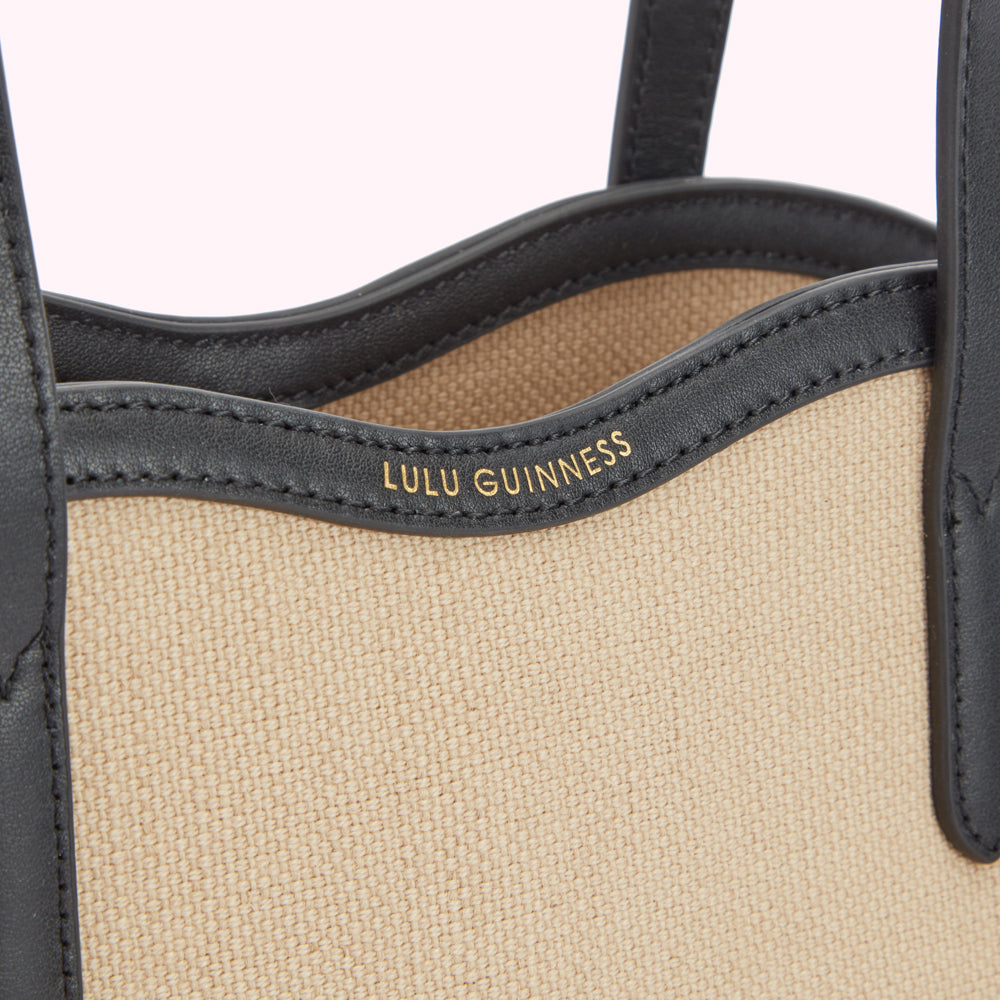 Detail close up image of a beige canvas and black leather tote bags foil print 'Lulu Guinness' logo.
